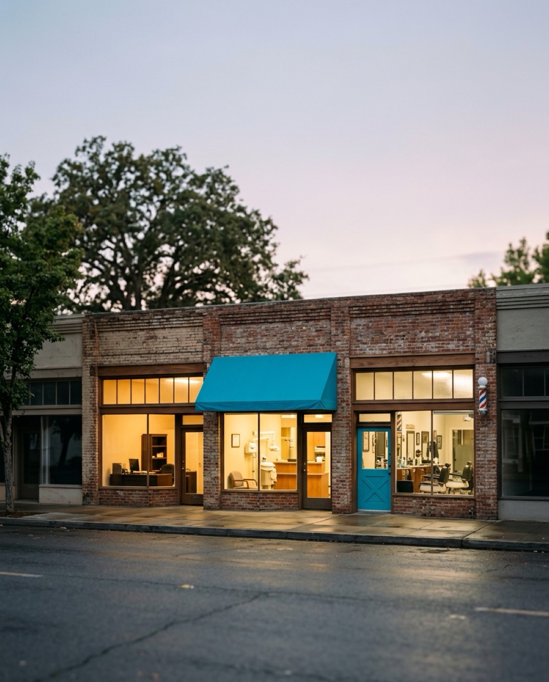 A small brick storefront with a blue awning at dusk
