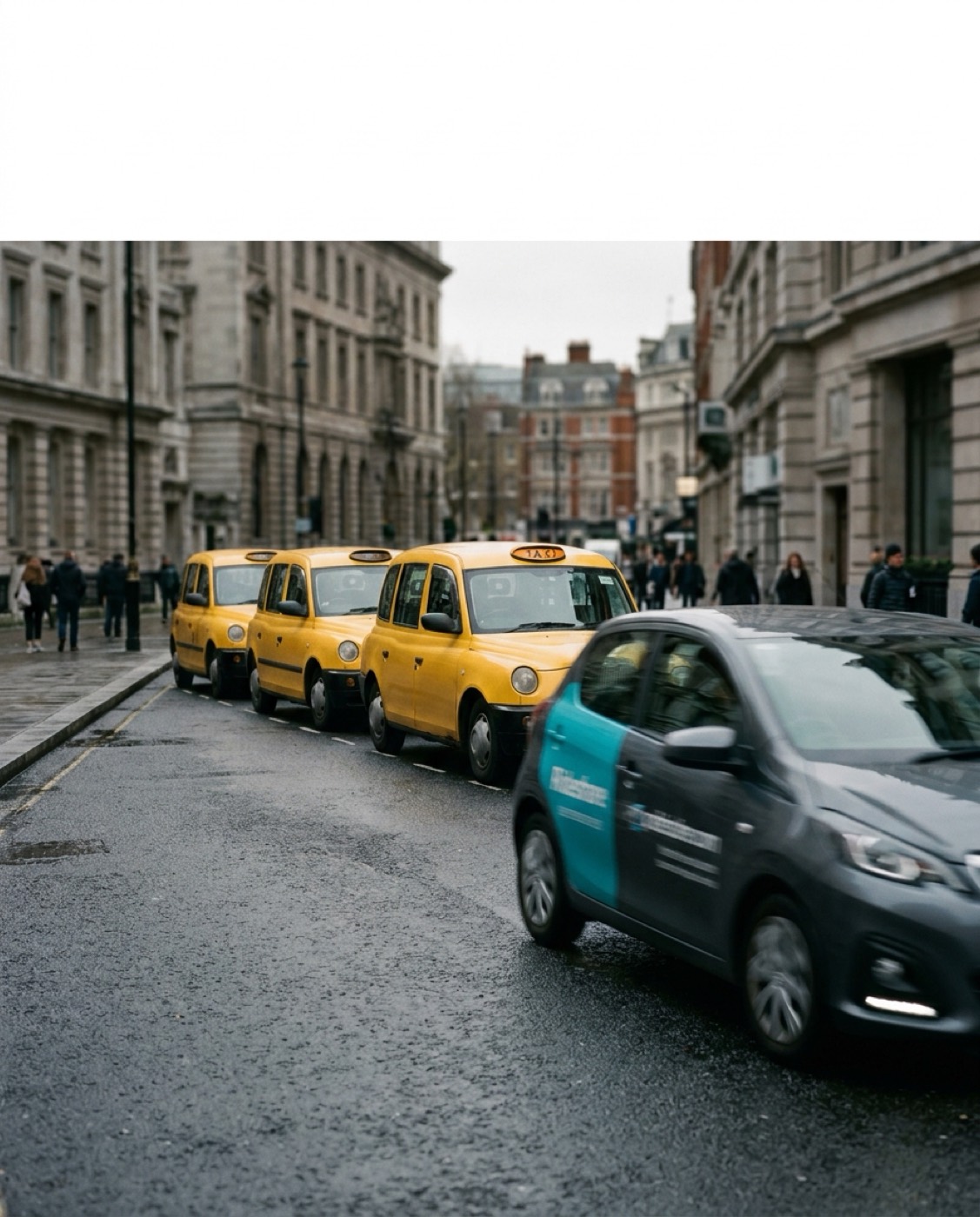A line of parked taxis on a wet street as a ride-share car passes them